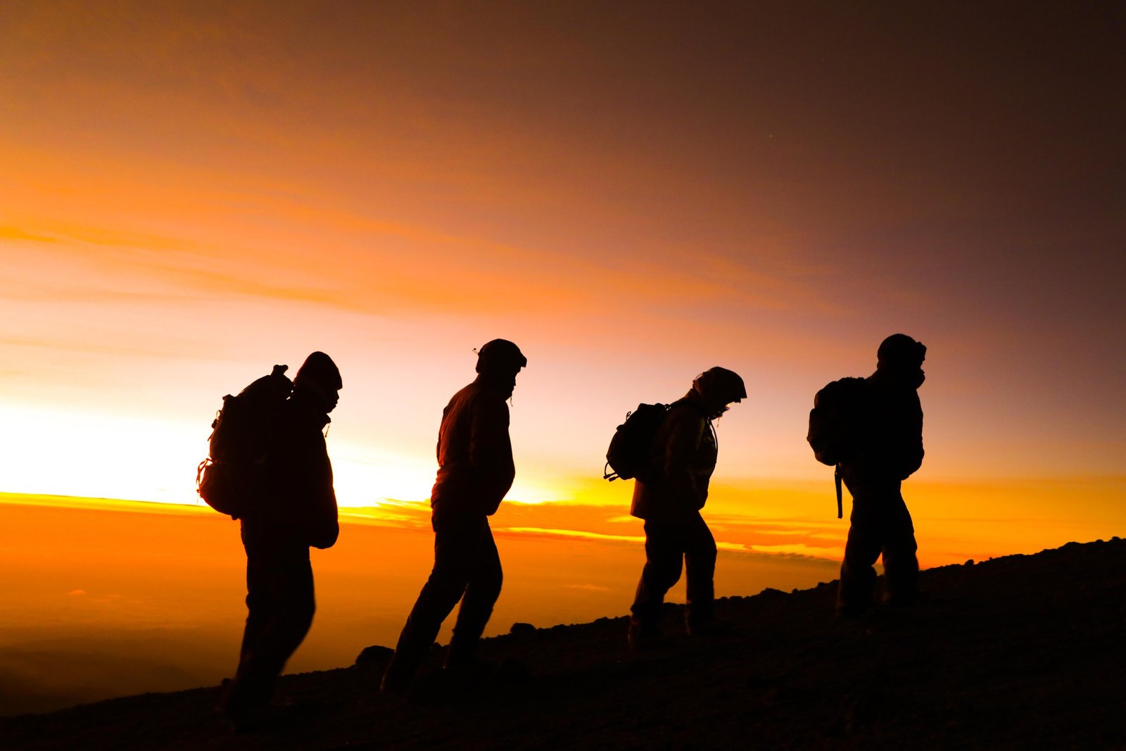 Climbers silhouetted against a vivid orange sky on Kilimanjaro